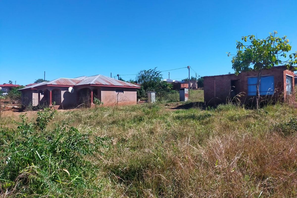 A residential plot featuring a main dwelling and a separate outbuilding structure, surrounded by undeveloped land with natural vegetation.