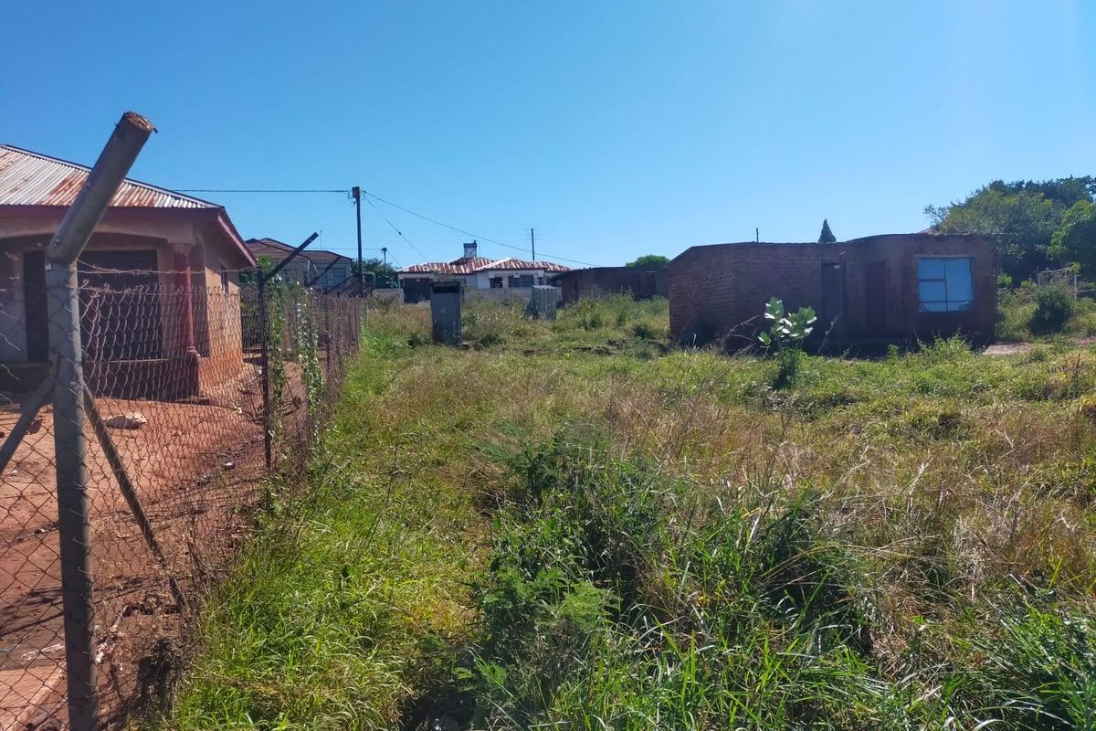 A view of a residential plot featuring overgrown grass, existing boundary fencing, and basic outbuildings on the property.