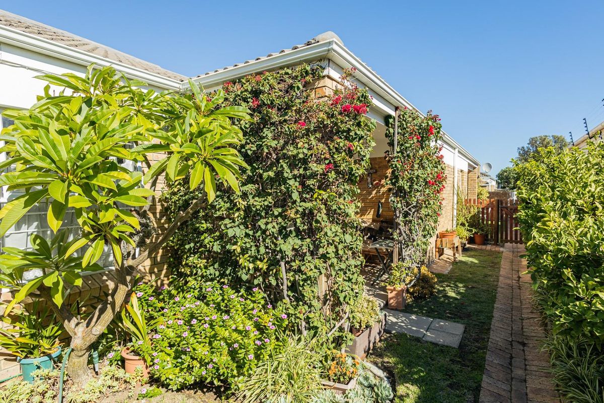 A well-maintained rear exterior view featuring a covered patio area, brick facade, and established garden landscaping with paved pathways.