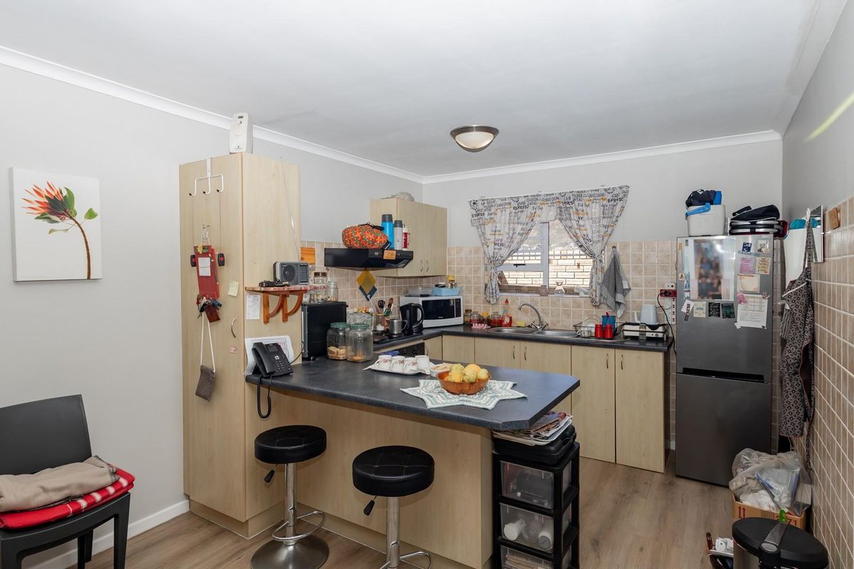 A functional kitchen featuring laminate cabinetry, a breakfast bar, tiled splashbacks, and a stainless steel sink, offering a practical layout for daily use.