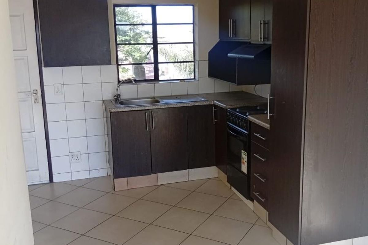 A functional kitchen featuring dark wood cabinetry, granite countertops, built-in oven, extractor fan, and tiled flooring, offering a clean and practical workspace.
