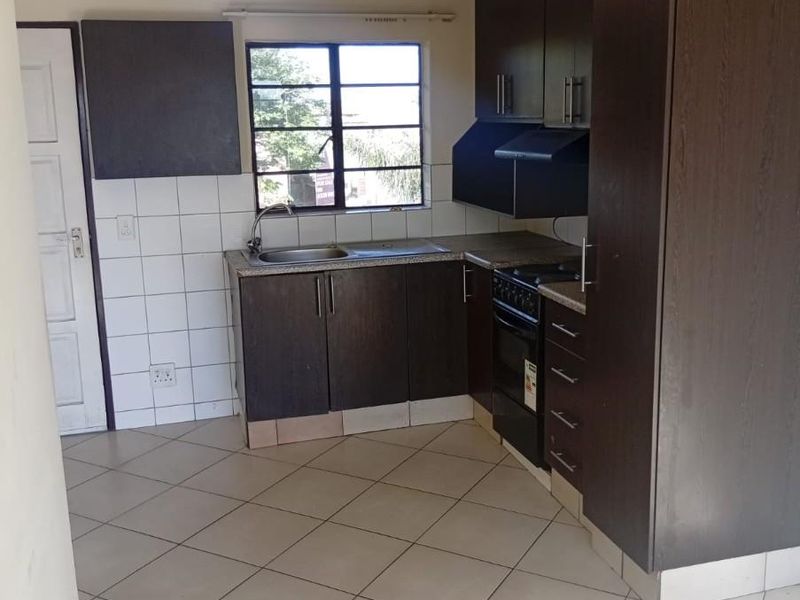 A functional kitchen featuring dark wood cabinetry, granite countertops, built-in oven, extractor fan, and tiled flooring, offering a clean and practical workspace.