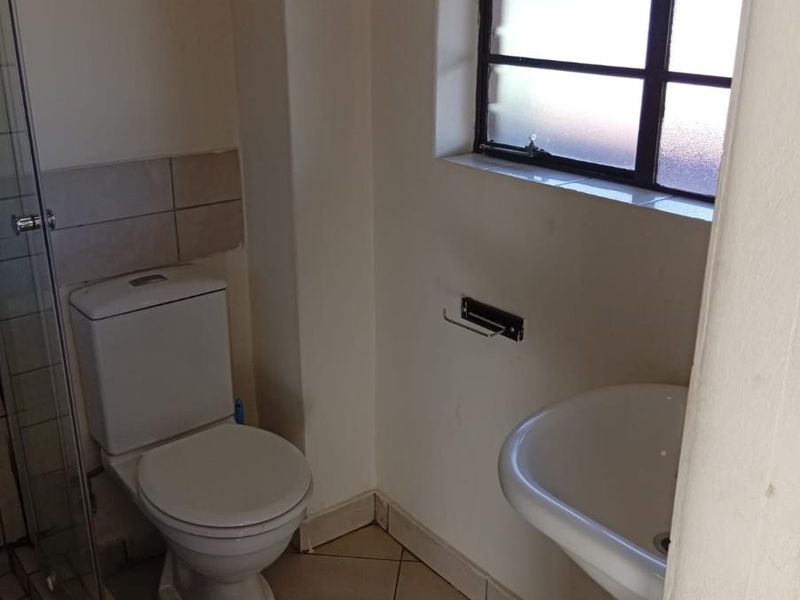 A compact bathroom featuring a pedestal basin, toilet, and shower enclosure with tiled flooring and a steel-framed window.