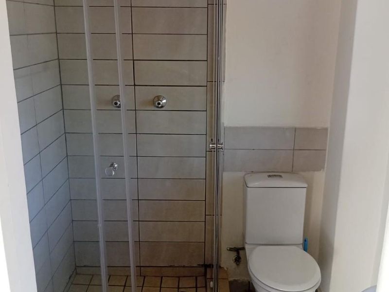 A functional bathroom featuring a glass-enclosed shower and a standard toilet with neutral wall and floor tiling.