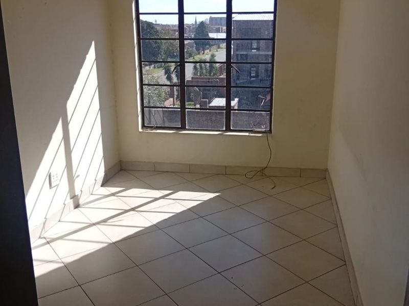 An empty bedroom featuring tiled flooring and a large steel-framed window with natural light, ready for personalization.