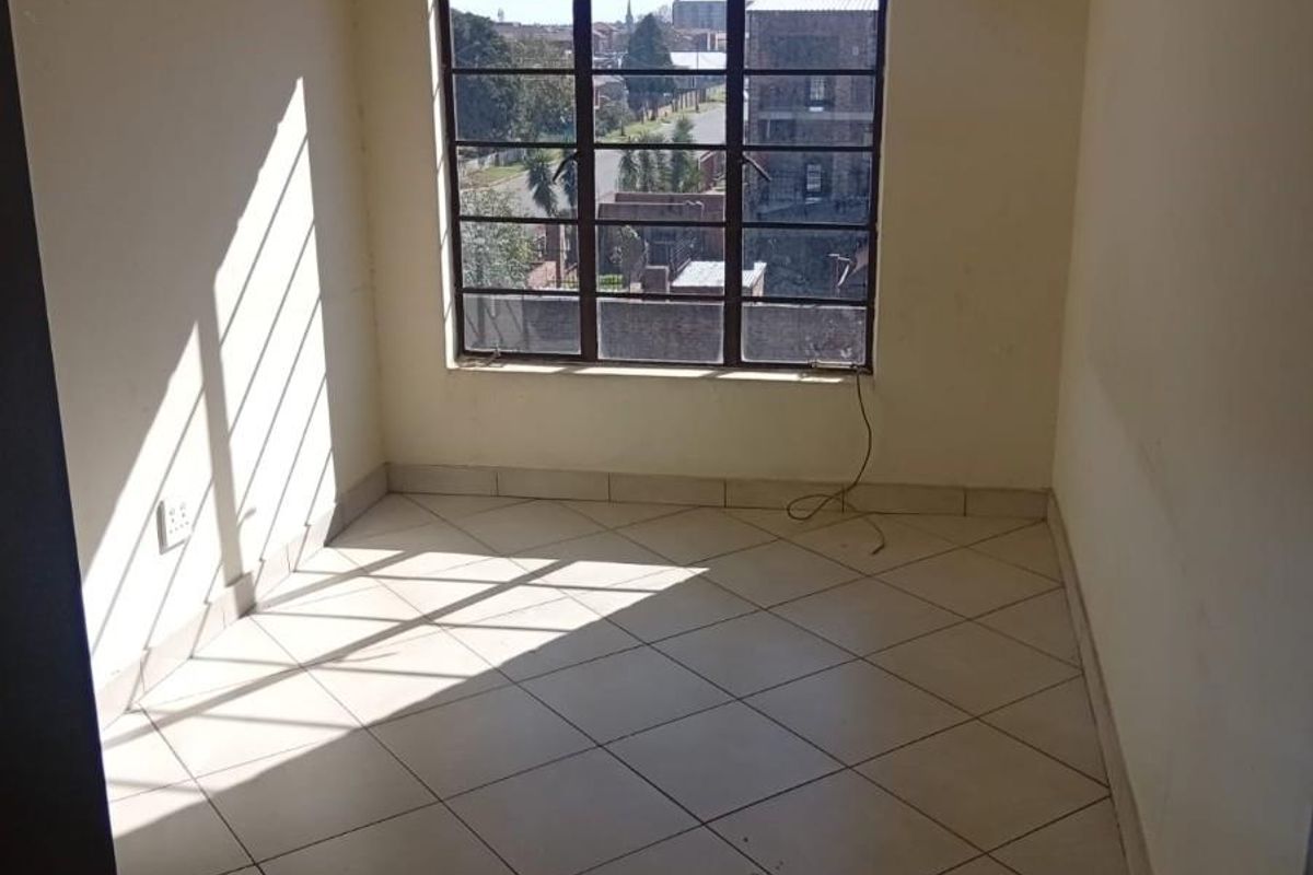 An empty bedroom featuring tiled flooring and a large steel-framed window with natural light, ready for personalization.