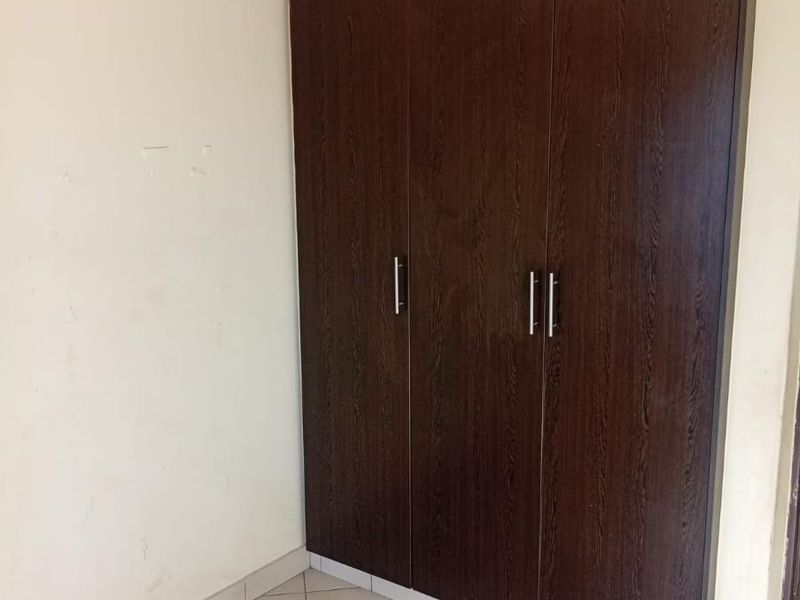 A bedroom featuring a dark wood built-in wardrobe and neutral tiled flooring, providing a clean and functional storage space.