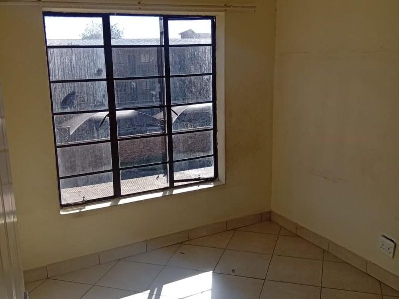 An empty bedroom featuring tiled flooring, a steel-framed window, and a ceiling light fixture, ready for personalization and cosmetic updates.