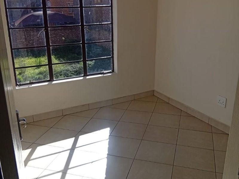 A bright, empty bedroom featuring neutral ceramic floor tiles, a large steel-framed window, and clean white walls, ready for personalization.