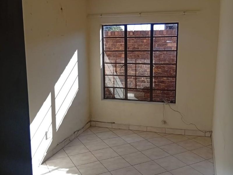 An empty bedroom featuring tiled flooring, a metal-framed window, and a ceiling light fixture, ready for renovation or staging.