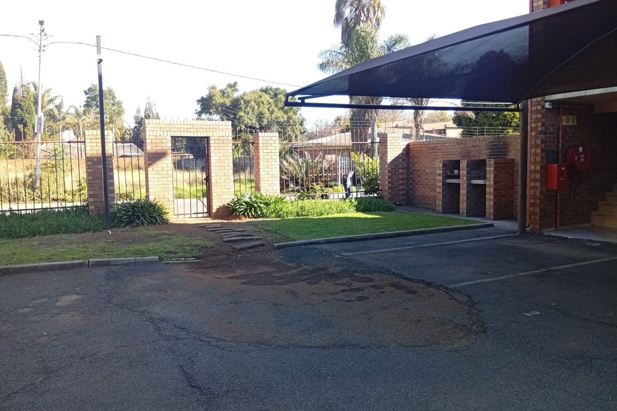 Rear exterior area featuring a paved driveway, shade cloth carport, built-in brick braai, and a secure brick boundary wall with pedestrian access.