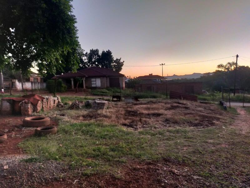 A view of the rear exterior grounds featuring a brick building with a tiled roof, surrounded by open land and mature trees at sunset.