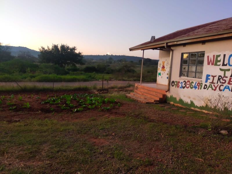 Exterior view of a single-story building with a corrugated roof, concrete steps, and a small garden area, currently utilized as a daycare facility.