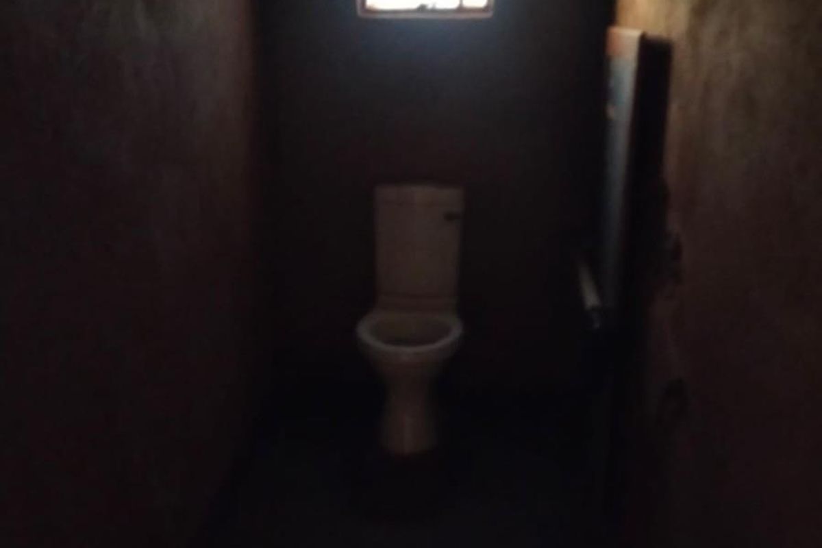 A small, dimly lit bathroom featuring a standard toilet and a single window, requiring significant renovation and improved lighting.