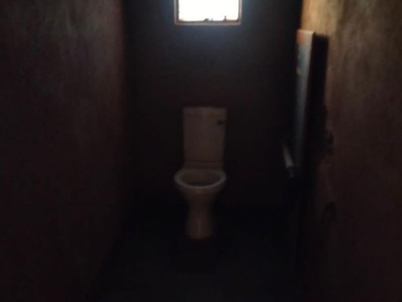 A small, dimly lit bathroom featuring a standard toilet and a single window, requiring significant renovation and improved lighting.