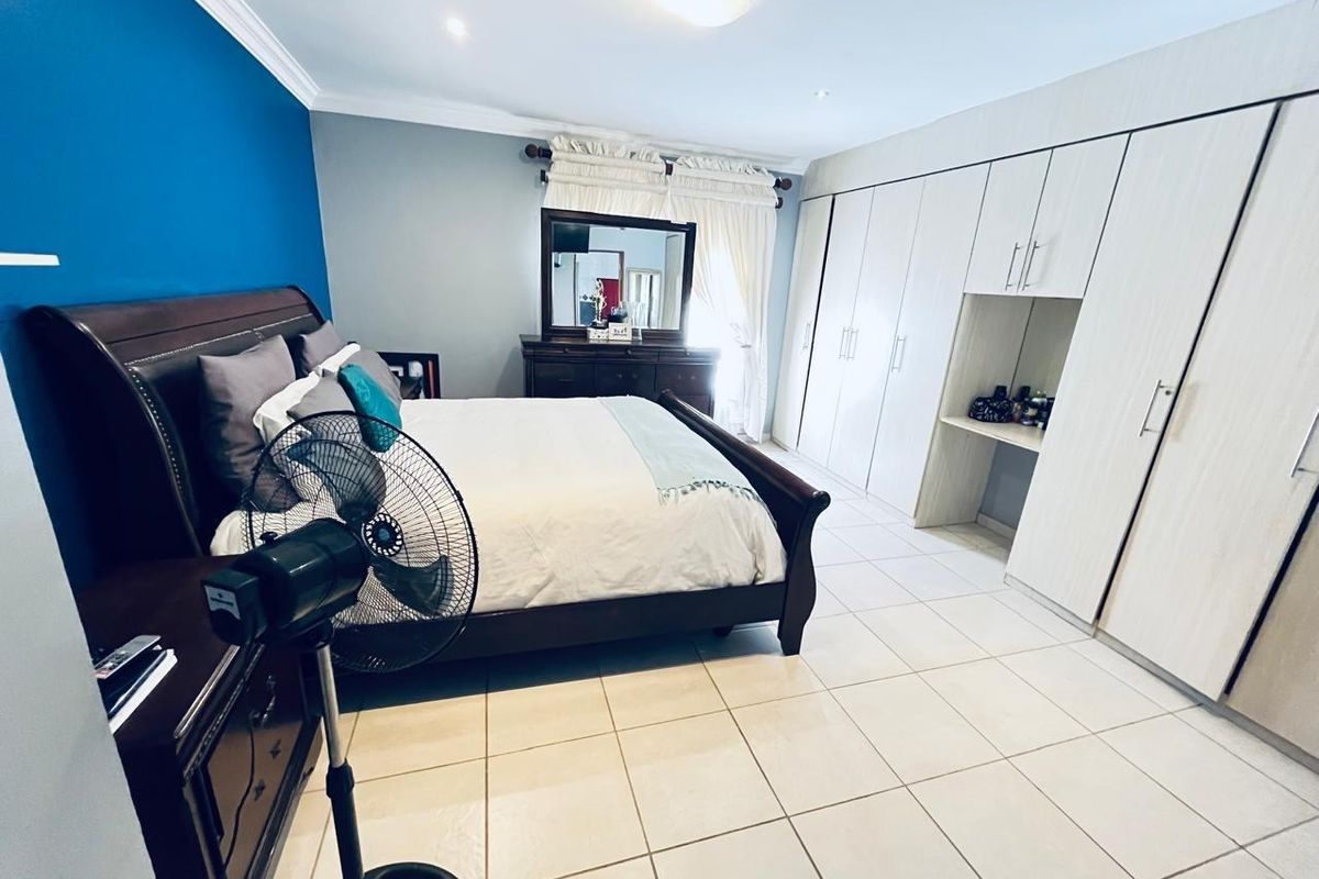 A spacious bedroom featuring built-in floor-to-ceiling wardrobes with integrated vanity desk, tiled flooring, and crown molding.