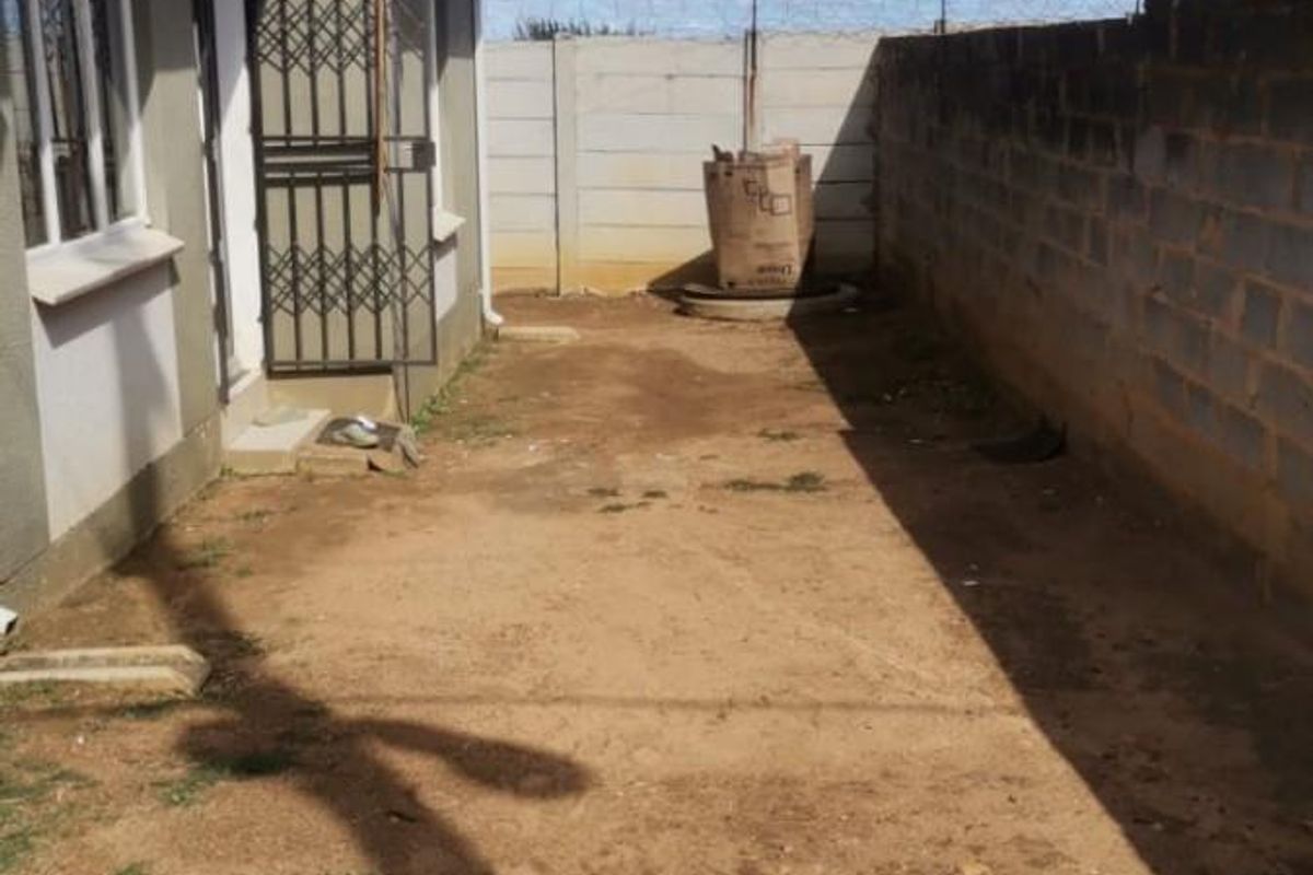 A side exterior view of the property featuring a narrow, unpaved yard area enclosed by a boundary wall with security wire.