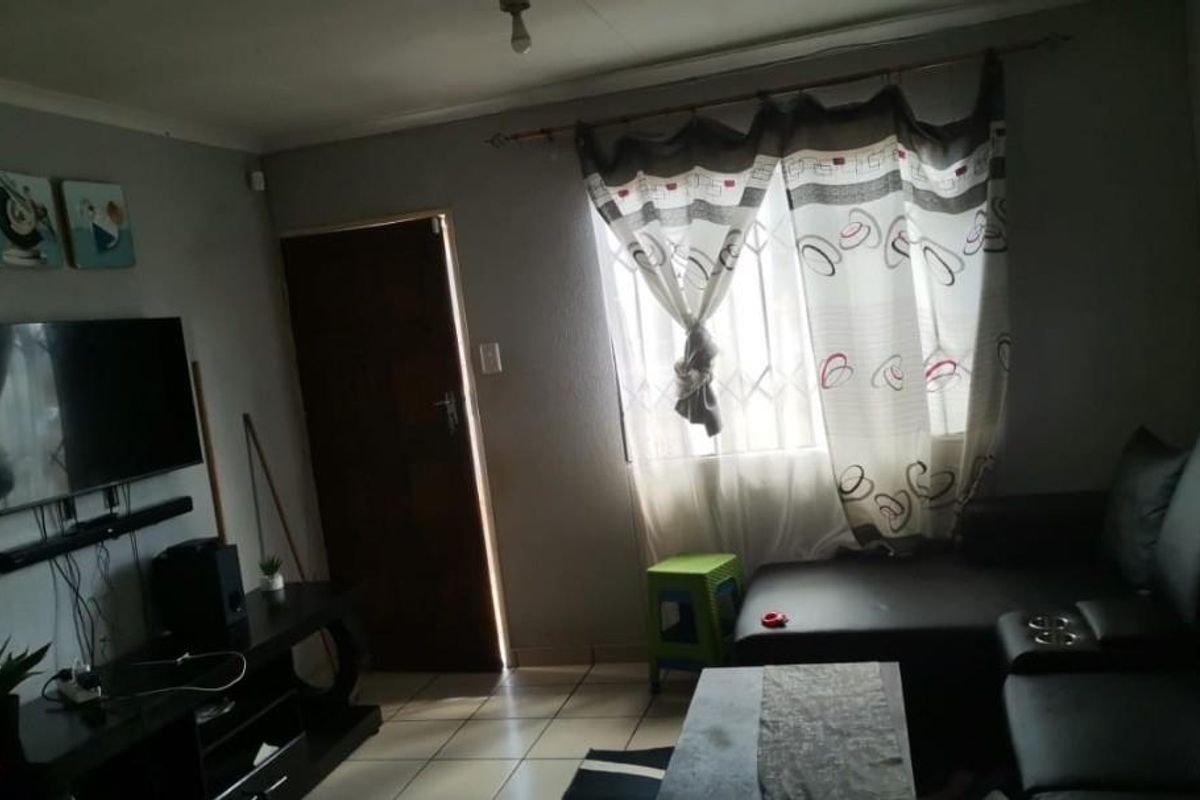 A functional living room featuring tiled flooring, a window with security bars, and a standard interior door.