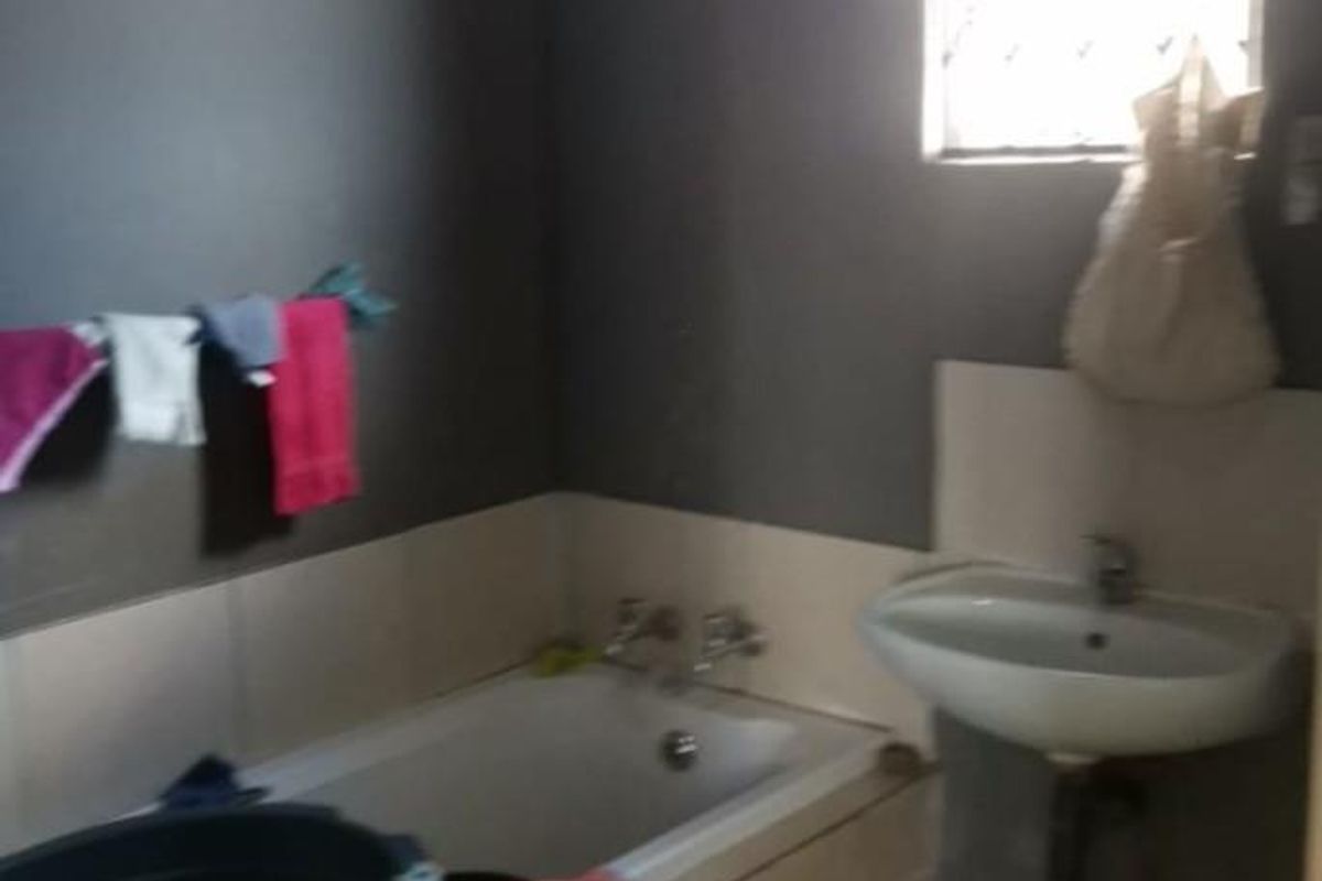 A functional bathroom featuring a built-in bathtub, wall-mounted basin, and tiled flooring, providing essential sanitary facilities.