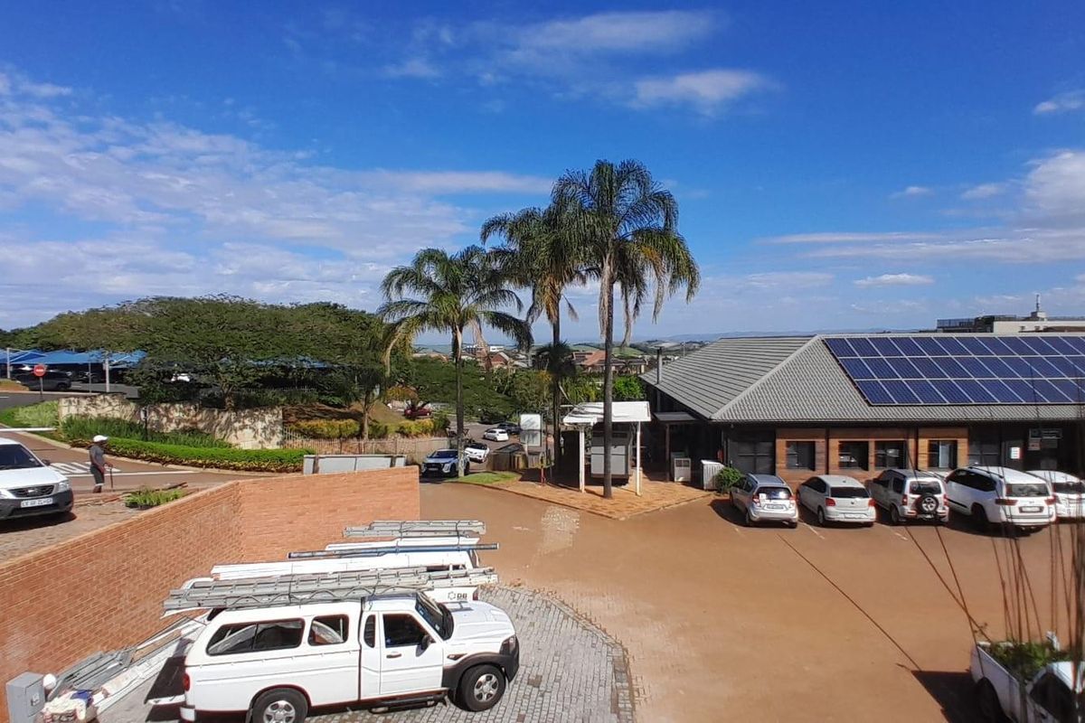 Elevated view of a commercial property exterior featuring a paved parking area, brick boundary walls, and a building roof equipped with solar panels.