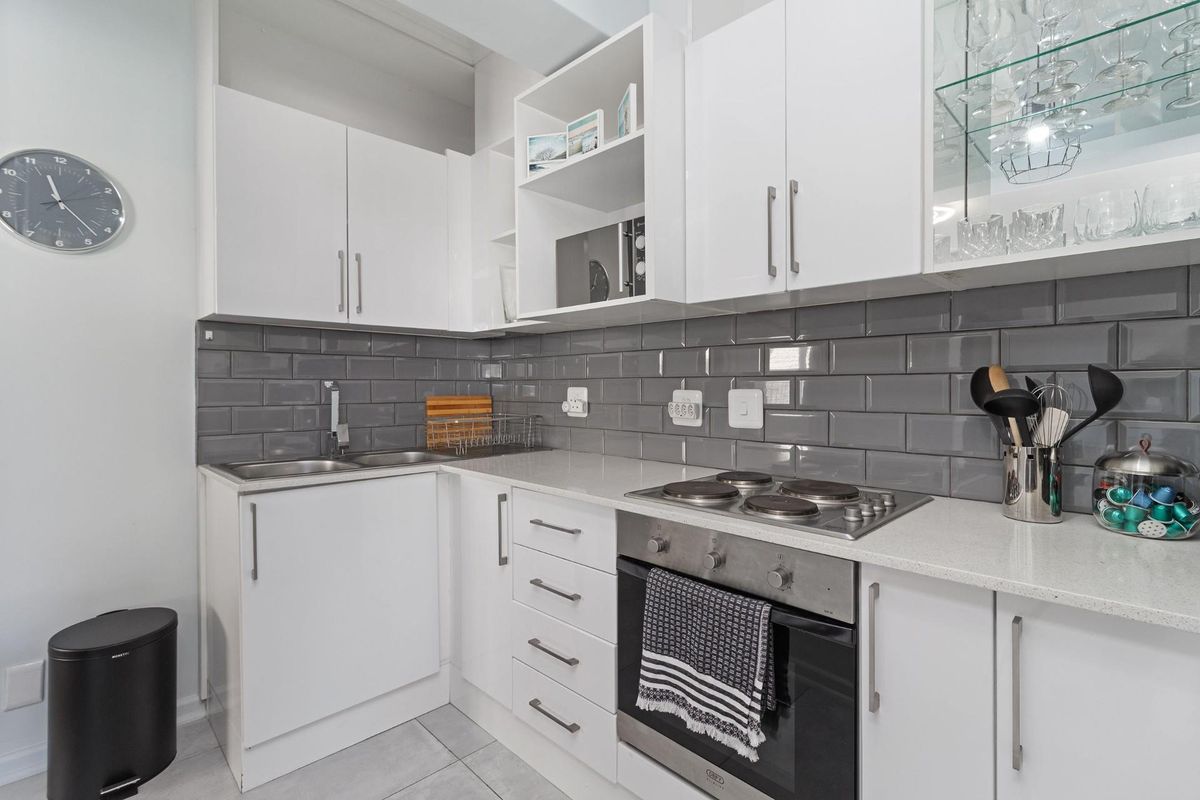 Modern kitchen featuring white cabinetry, grey subway tile backsplash, integrated electric hob, built-in oven, and a glass-fronted display cabinet.