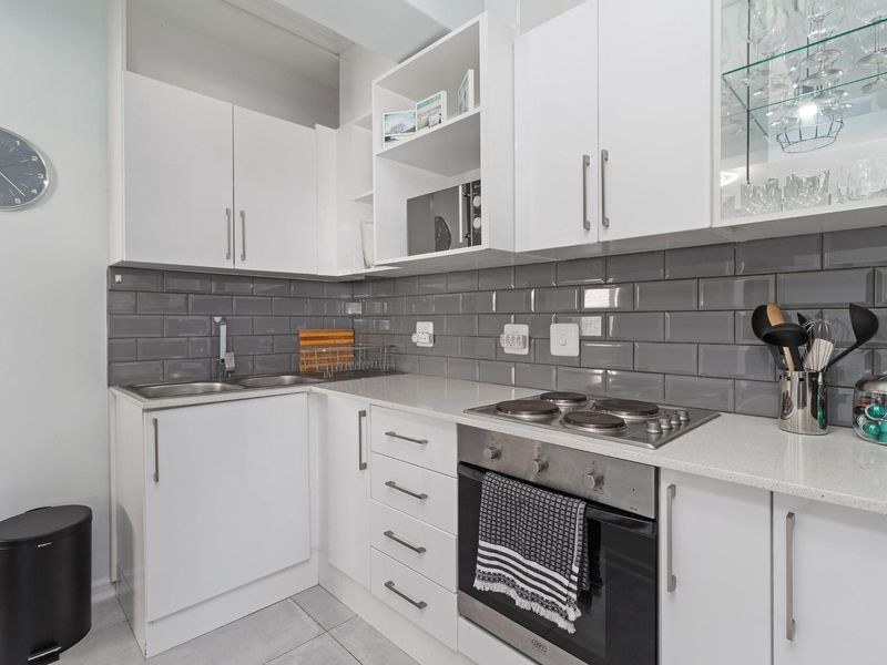 Modern kitchen featuring white cabinetry, grey subway tile backsplash, integrated electric hob, built-in oven, and a glass-fronted display cabinet.