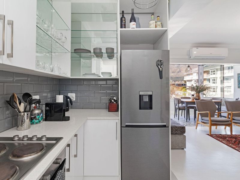 Modern open-plan kitchen featuring sleek white cabinetry, grey subway tile backsplash, stone countertops, and integrated appliances, flowing into the adjacent living and dining area.