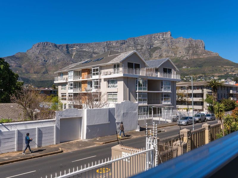 Elevated view of a modern apartment building set against the backdrop of Table Mountain, featuring balconies and secure perimeter fencing.