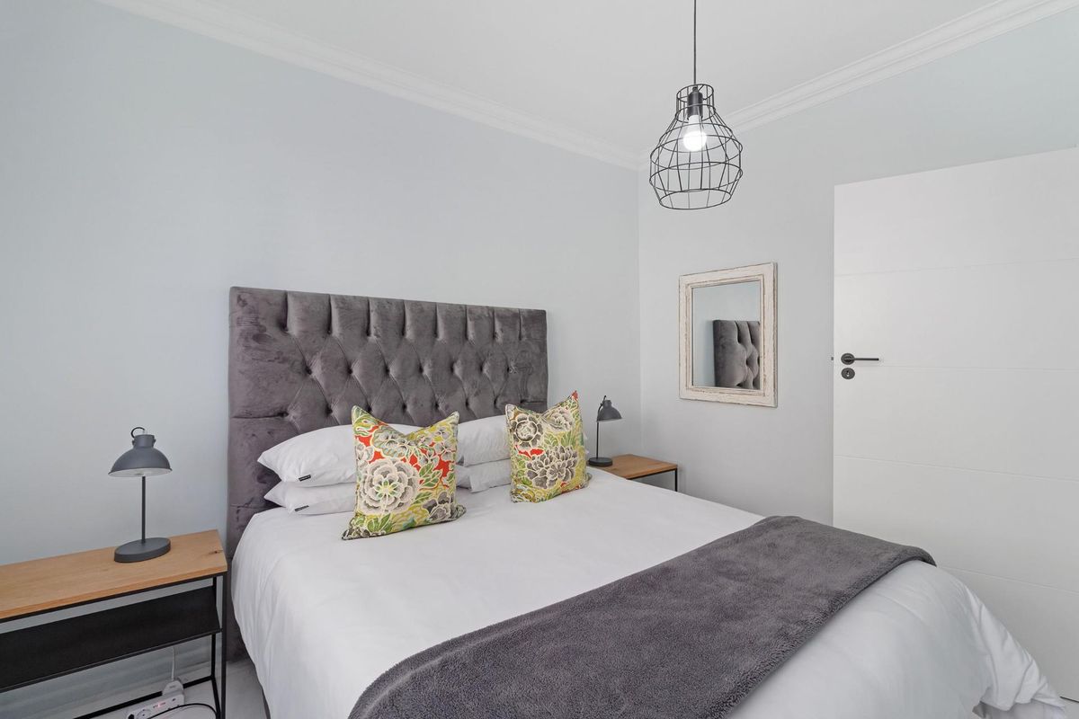 A well-maintained bedroom featuring neutral walls, cove cornicing, and a modern pendant light fixture.