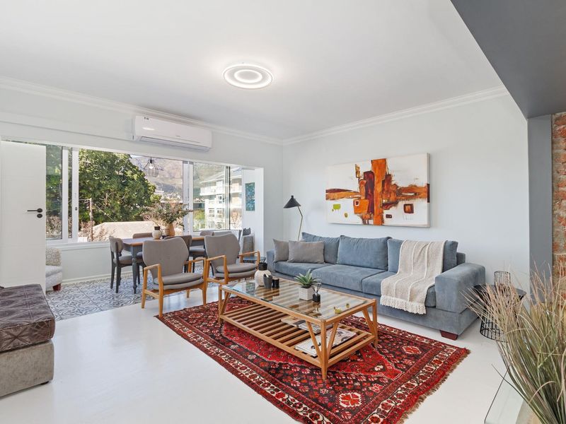 Bright open-plan living and dining area featuring an exposed brick accent wall, modern air conditioning, and large windows with natural light.
