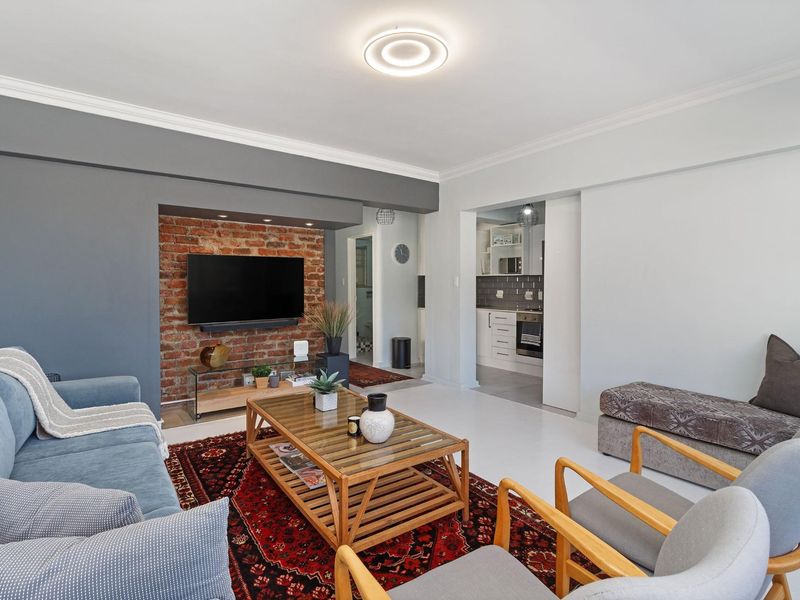 Open-plan living area featuring an exposed brick feature wall, neutral tiled flooring, and a seamless transition to a modern, well-equipped kitchen.