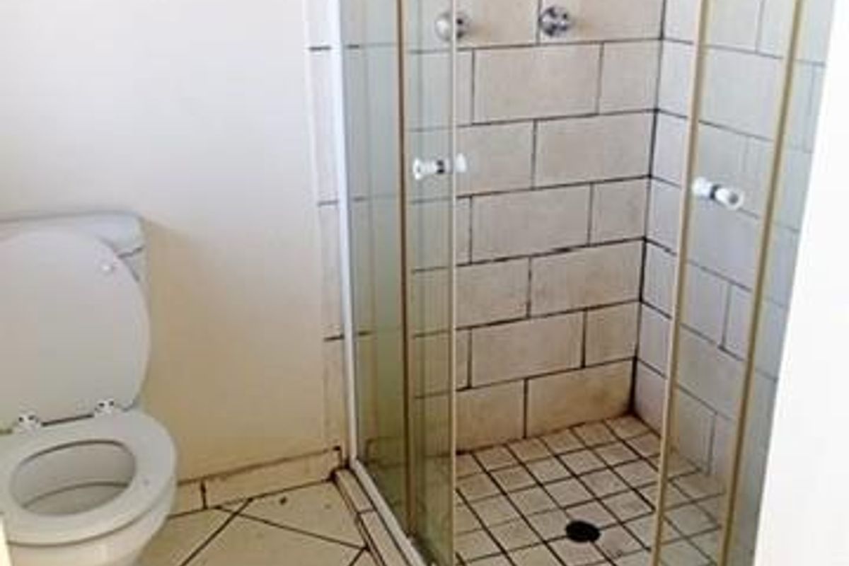 A functional bathroom featuring a shower enclosure and toilet, with tiled flooring and walls. The space requires cosmetic updates and maintenance.