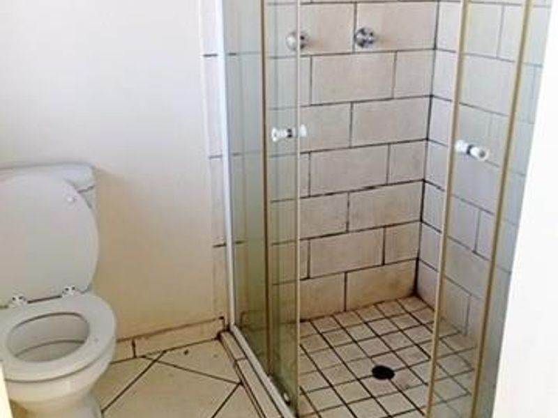 A functional bathroom featuring a shower enclosure and toilet, with tiled flooring and walls. The space requires cosmetic updates and maintenance.