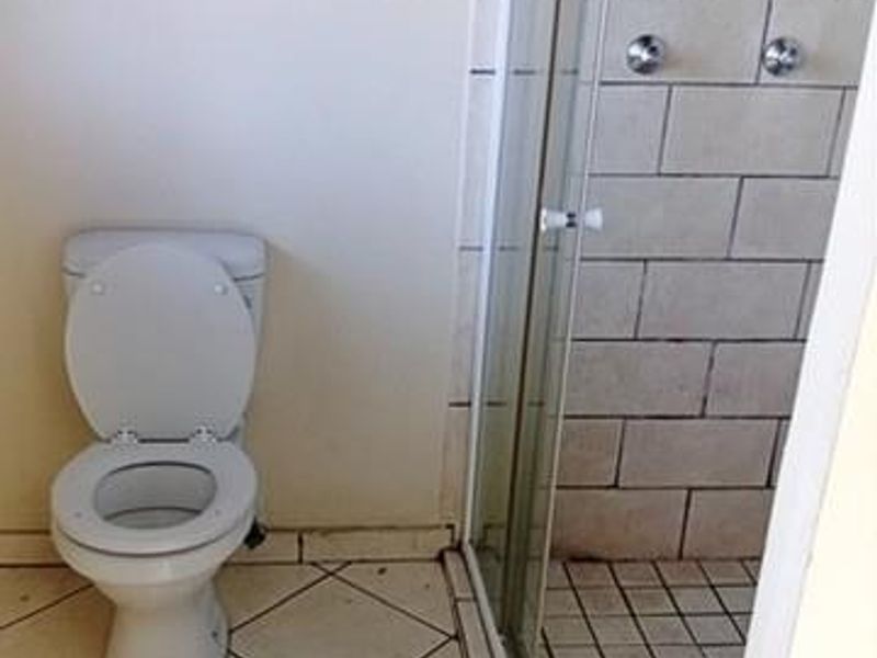 A functional bathroom featuring a standard toilet and a glass-enclosed shower with tiled finishes, requiring cosmetic updates to improve its overall condition.