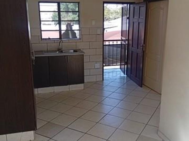 A compact kitchen area featuring built-in cabinetry, a sink, and tiled flooring, with direct access to an exterior balcony through a security gate.