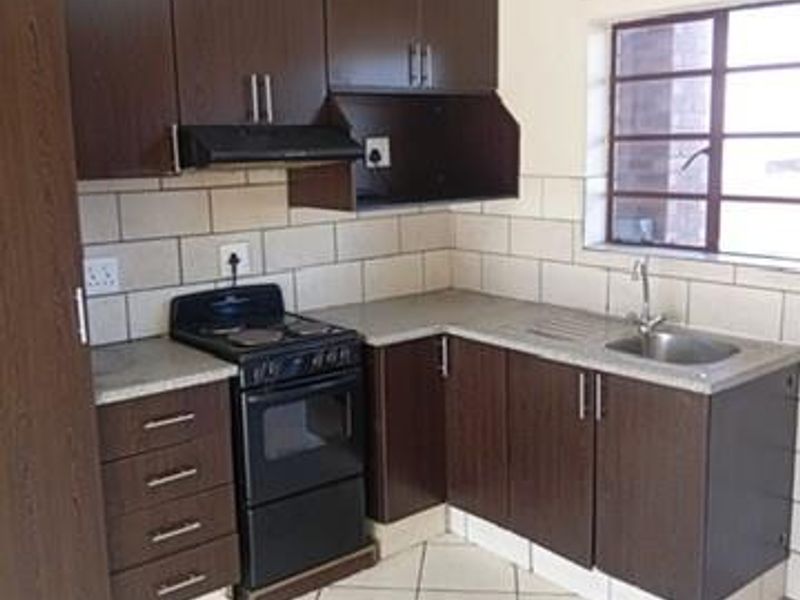 A functional kitchen featuring dark wood cabinetry, laminate countertops, a stainless steel sink, and a freestanding electric stove with an extractor fan.