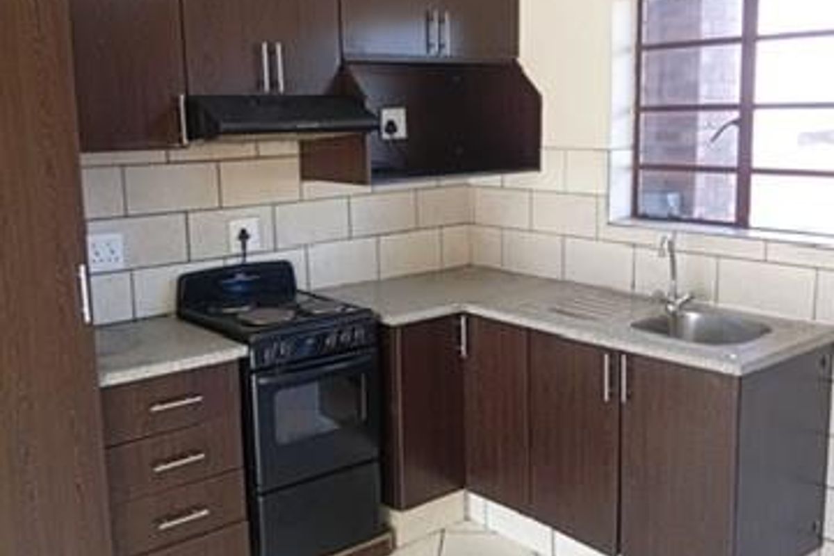 A functional kitchen featuring dark wood cabinetry, laminate countertops, a stainless steel sink, and a freestanding electric stove with an extractor fan.