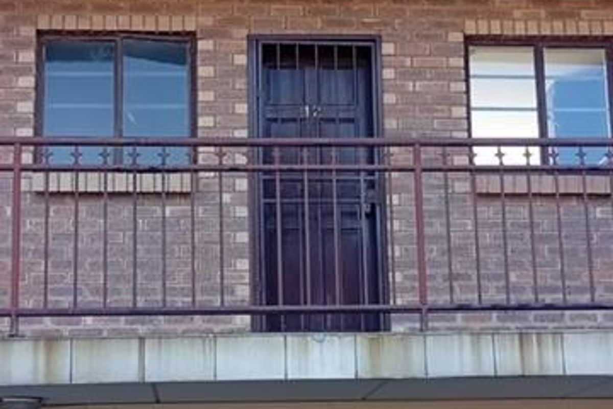 Exterior view of an apartment building facade featuring brickwork, metal security gates, and balcony access with visible wear on concrete and metal elements.