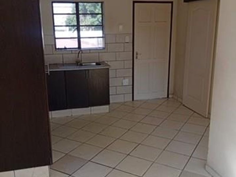 A compact, empty kitchen area featuring tiled flooring, a tiled splashback, built-in cabinetry with a sink, and two internal doors.