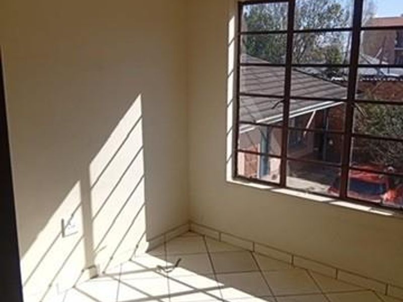 An empty bedroom featuring tiled flooring and a large steel-framed window allowing for natural light.