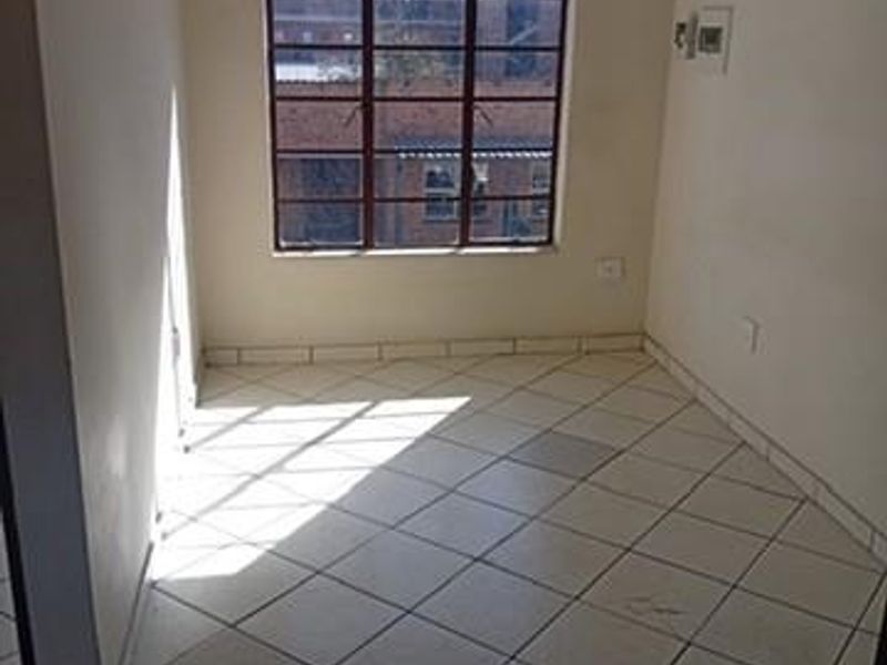 An empty bedroom featuring tiled flooring and a steel-framed window, providing a blank canvas for potential interior design updates.