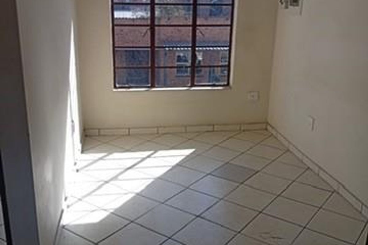 An empty bedroom featuring tiled flooring and a steel-framed window, providing a blank canvas for potential interior design updates.