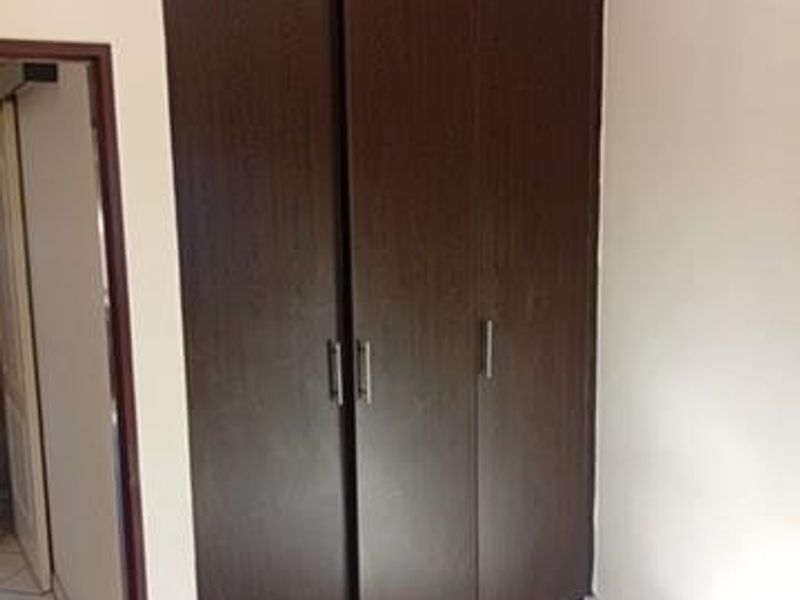 A bedroom featuring dark wood built-in cupboards and neutral tiled flooring, offering a clean and functional space.