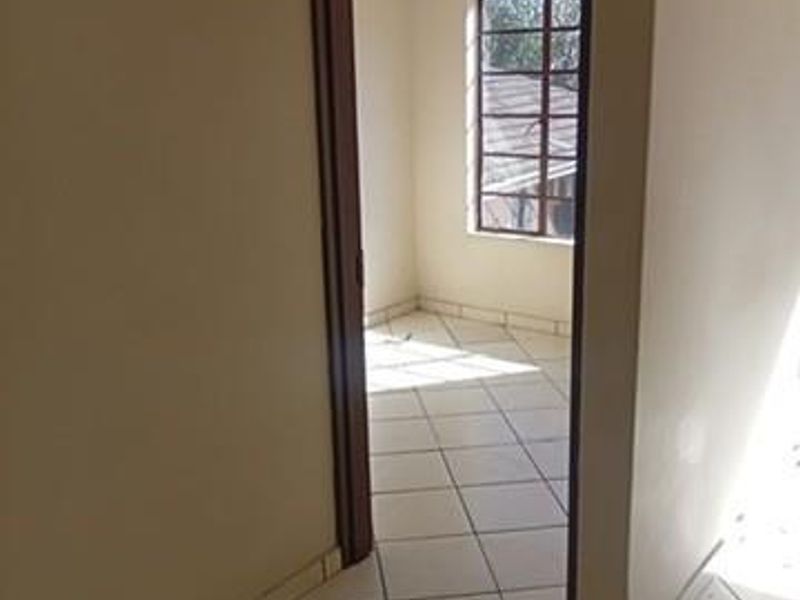 A vacant hallway with tiled flooring leading into an adjacent room featuring a window with security bars.