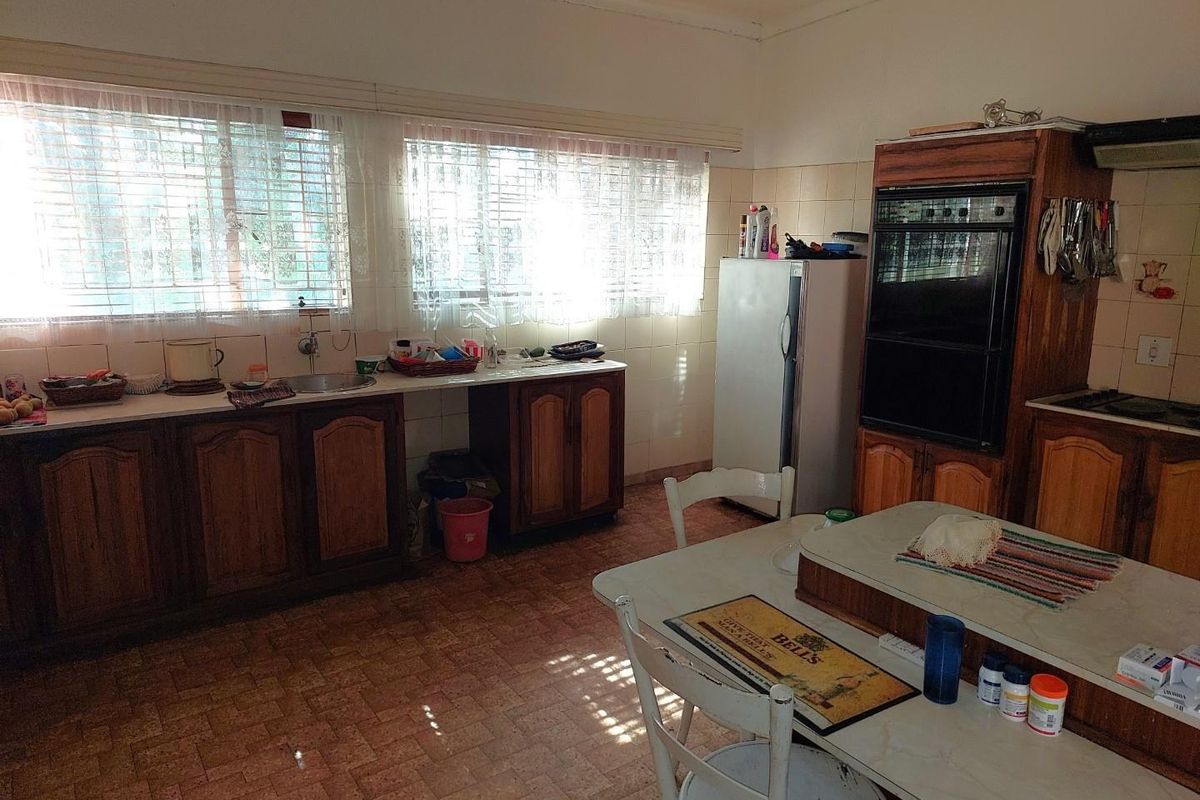 A dated kitchen featuring wooden cabinetry, built-in oven, and tiled flooring, offering a functional layout with ample natural light from large windows.