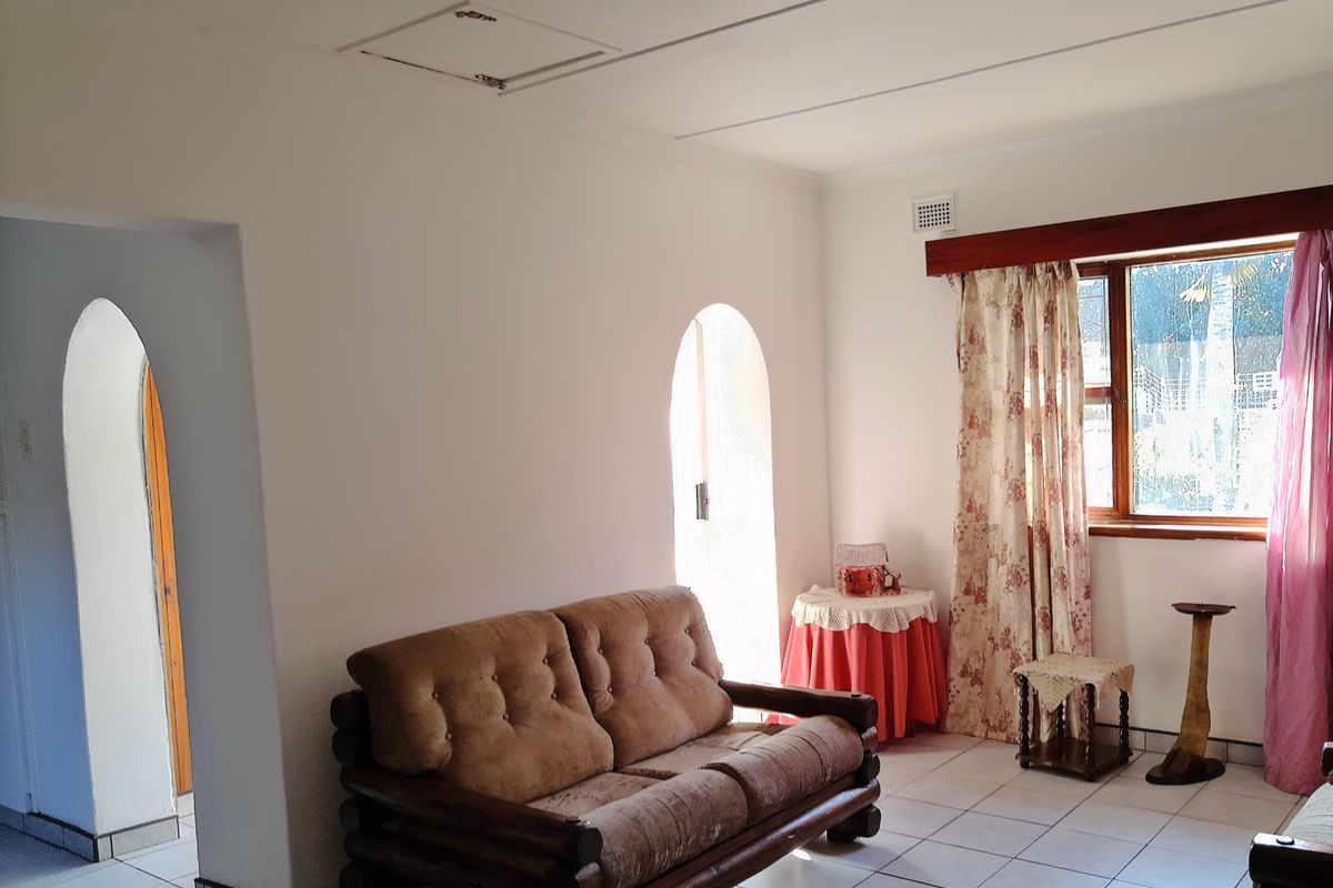 A living room featuring tiled flooring, arched doorways, and a window with wooden trim, providing a bright and functional living space.