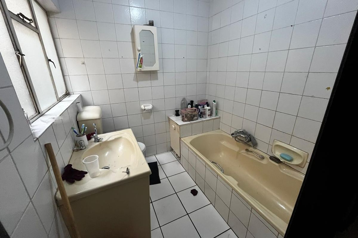 A dated bathroom featuring a built-in bathtub, vanity basin, and full-height wall tiling, offering potential for a modern renovation.