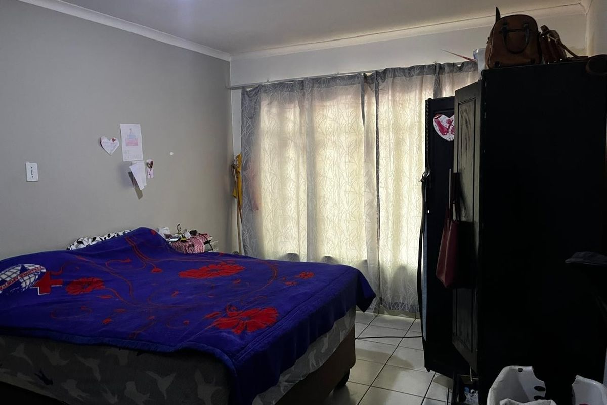 A bedroom featuring tiled flooring and large windows with curtains, providing natural light to the space.