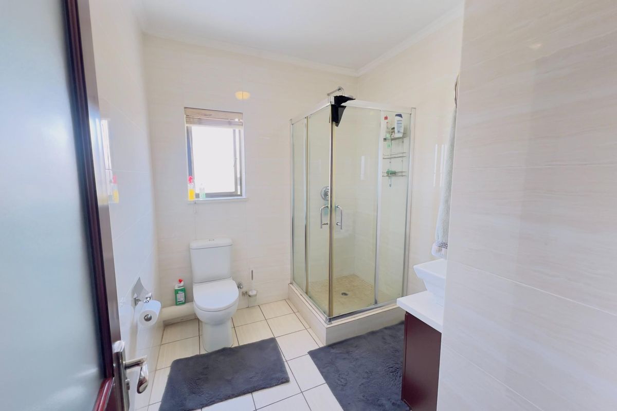 A functional bathroom featuring a glass-enclosed shower, a white toilet, and a vanity unit with a basin, finished with neutral wall and floor tiles.