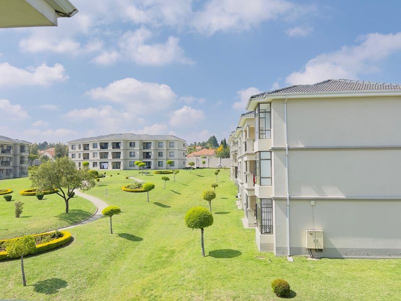 Elevated view of the apartment complex grounds, featuring well-maintained lawns, landscaped gardens, and paved walkways between residential buildings.